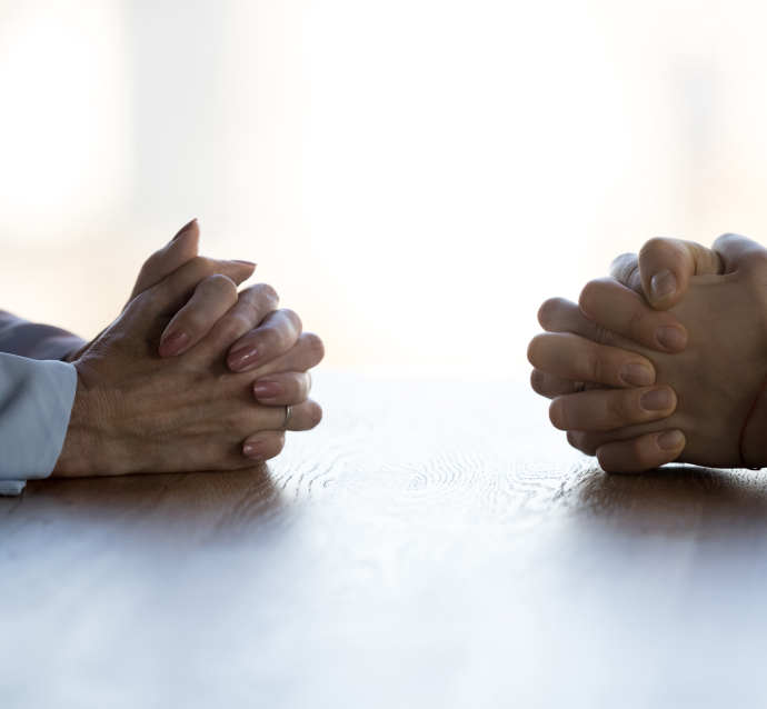 Folded hands facing each other from across the table, symbolizing attorneys negotiating a wrongful death claim