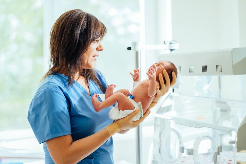 Health care concept. Doctor neonatologist calming down a crying baby holding newborn infant baby girl in hospital. Medical checkup.