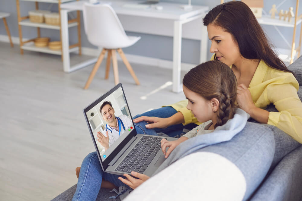 A male doctor online consults a diagnosis of symptoms to a mother and daughter through video chat using a laptop.